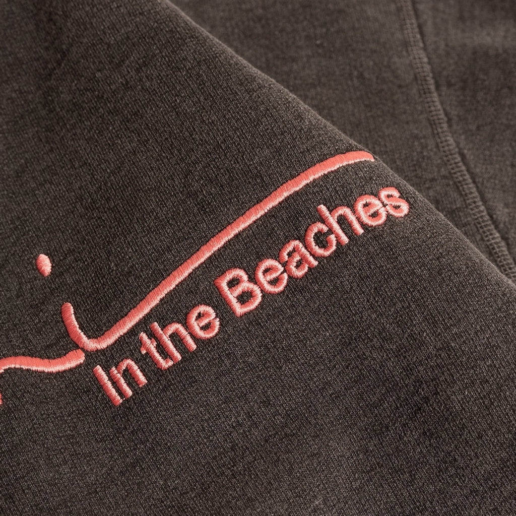 Close-up of a black fabric with 'In the Beaches' embroidered in pink.