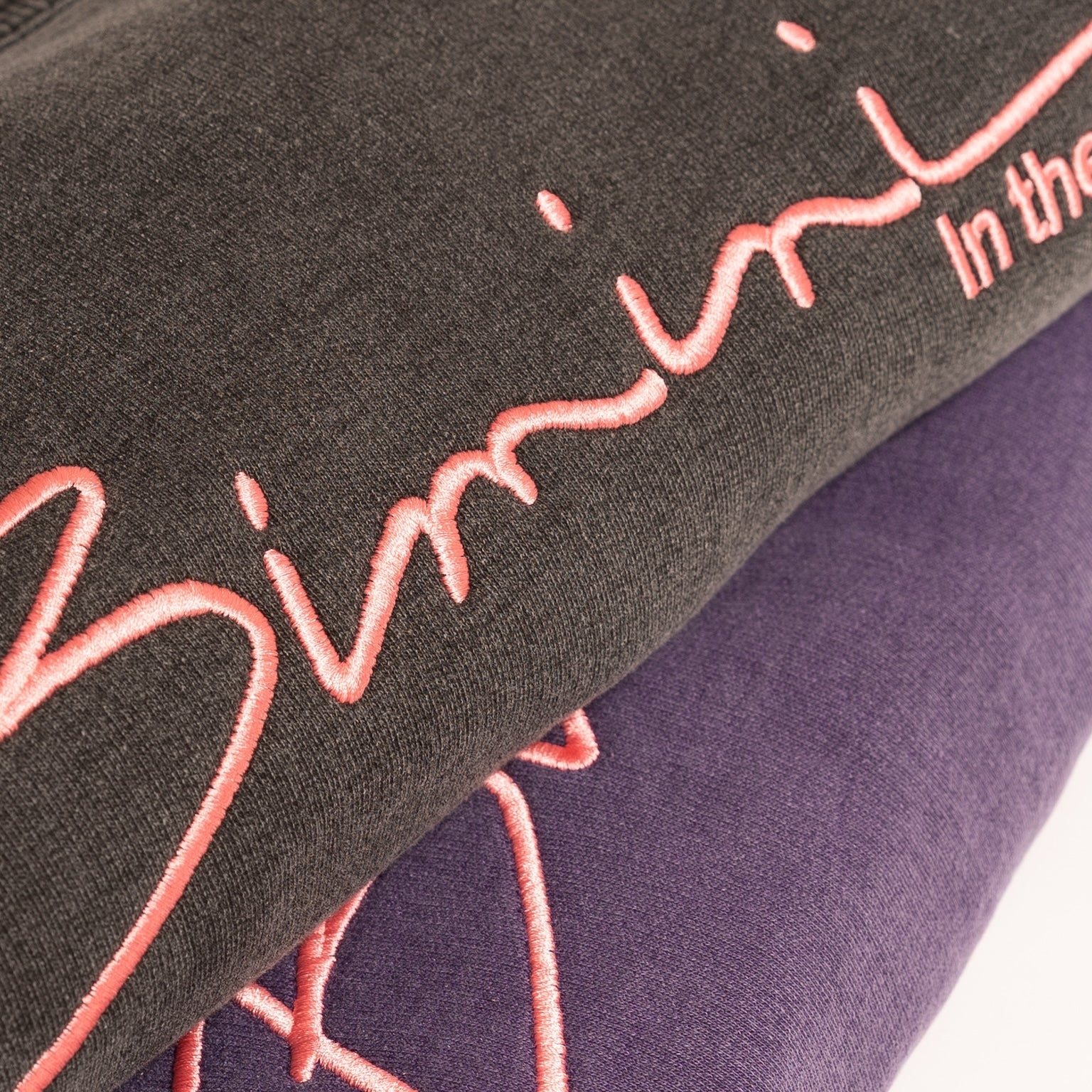 Close-up of 'Bimini' sweatshirts with pink embroidery on a dark background