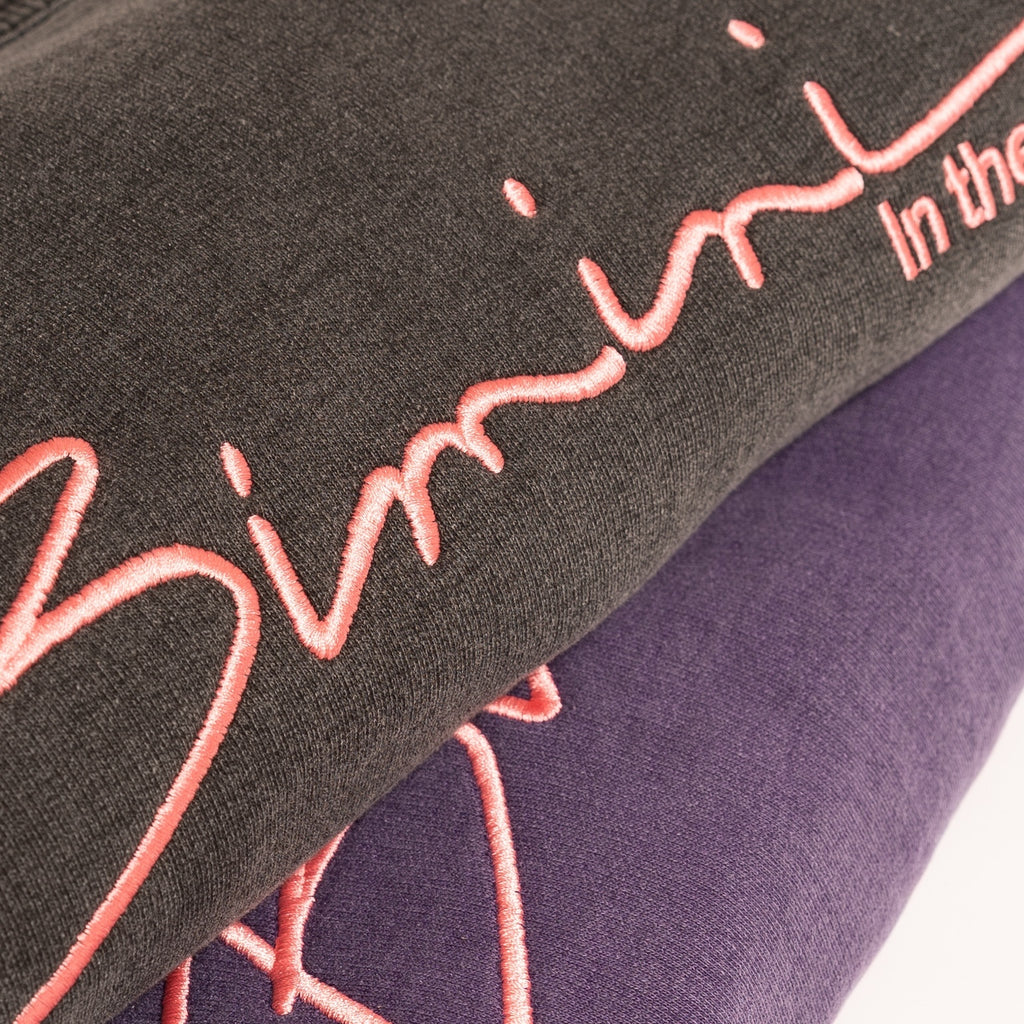 Close-up of 'Bimini' sweatshirts with pink embroidery on a dark background