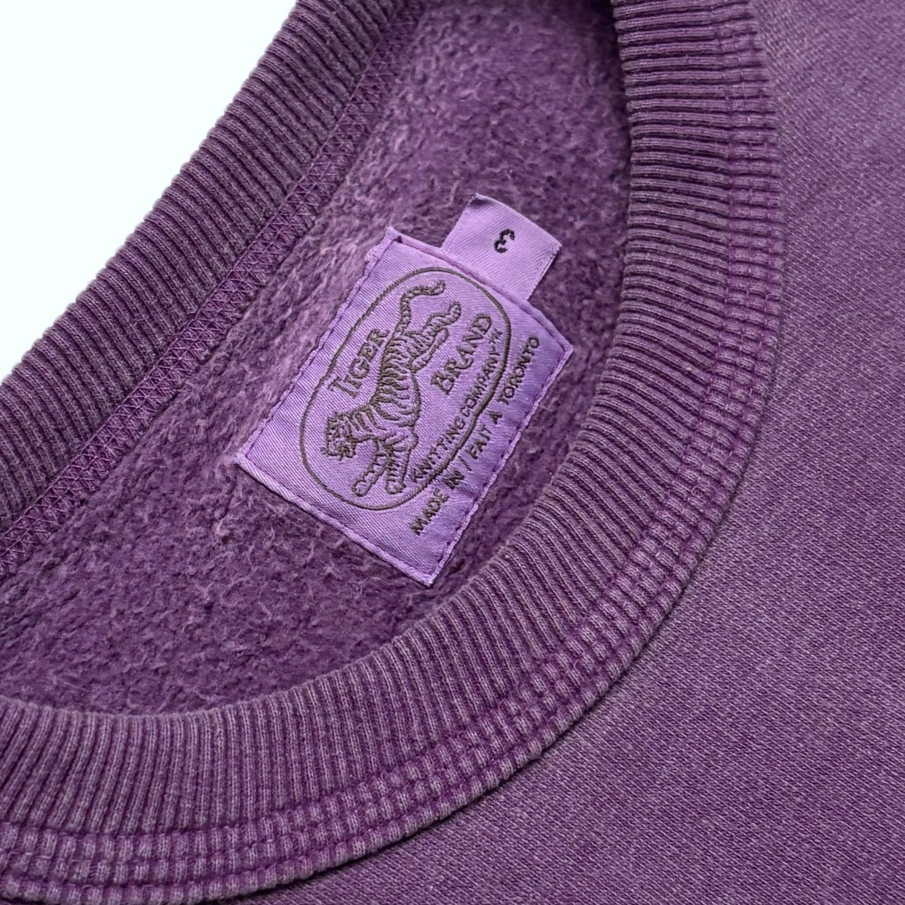 Close-up of a purple sweater with a brand label featuring a tiger logo.