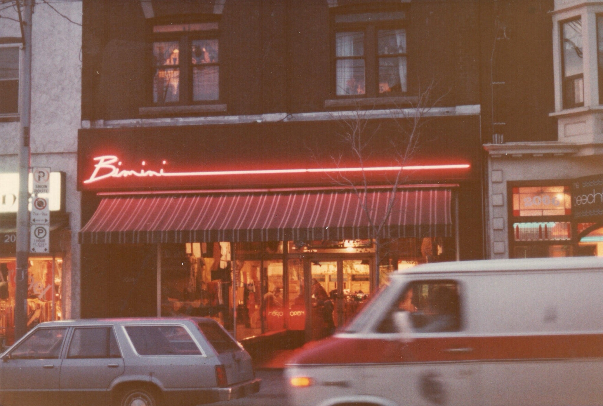 The Bimini storefront with a neon sign and cars moving in front