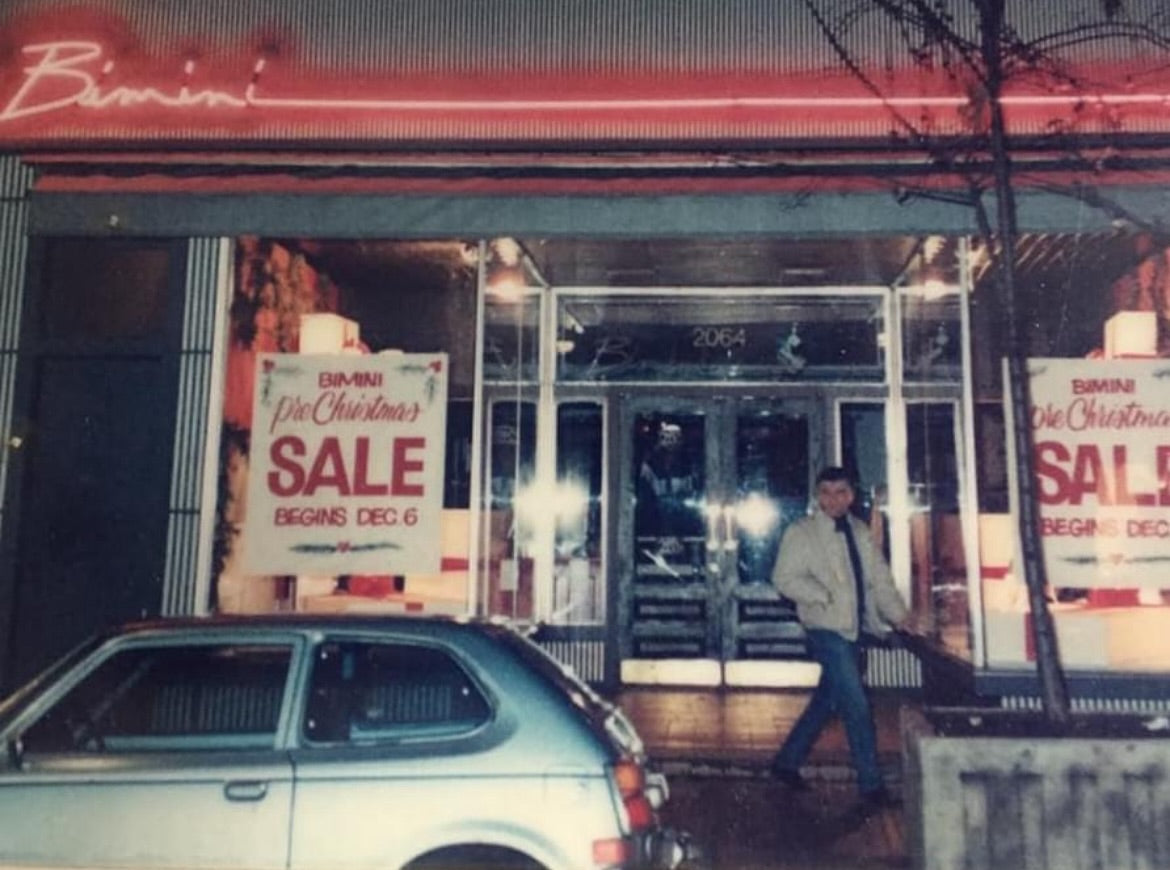 Vintage store front with 'Bimini' sign and 'SALE' signs, man walking by car.